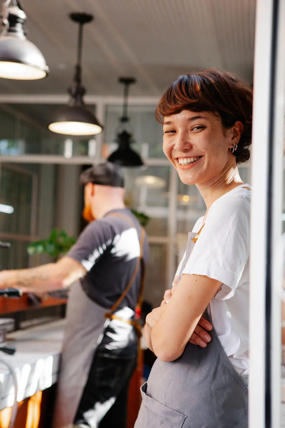 A café worker smiling in the doorway of a busy kitchen.